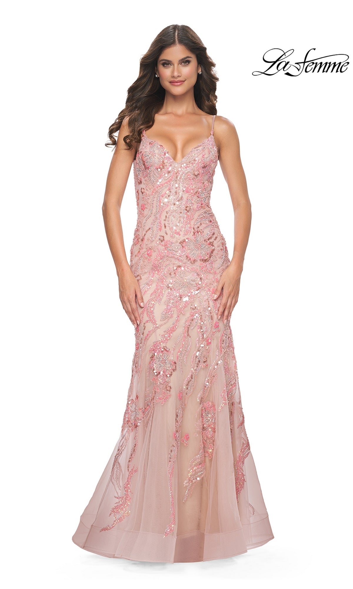 A woman in a fitted, coral Le Femme Long Sequin-Lace Prom Dress 32333 with thin straps stands facing forward. The gown features a sheer overlay and floral designs for an elegant, enchanting look.